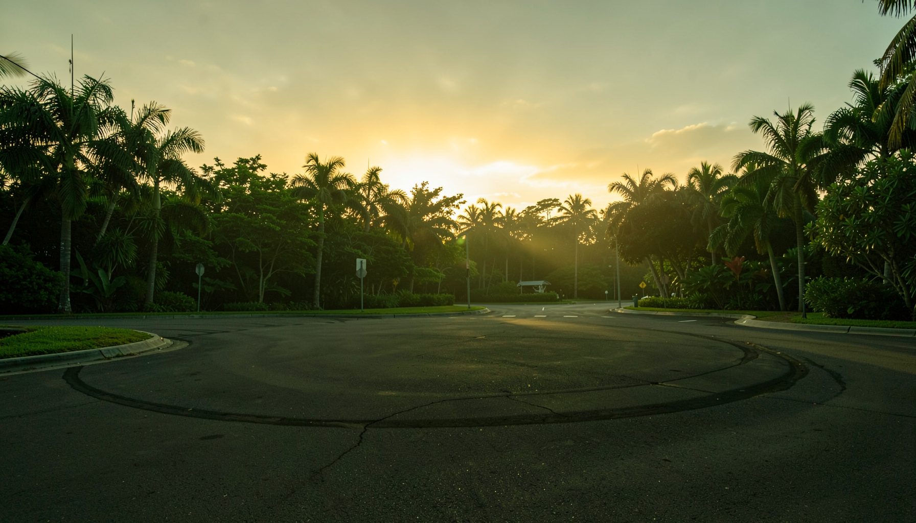 Sunset photograph of a roundabout at a Hawaiian intersection, golden sky overhead, empty asphalt and tropical greenery